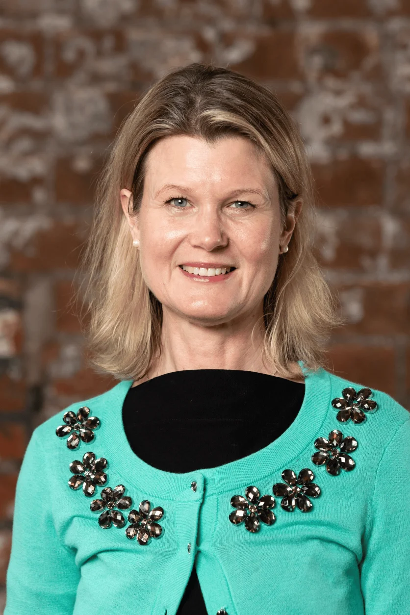 Photo of a woman smiling with blonde hair and a turquoise cardigan