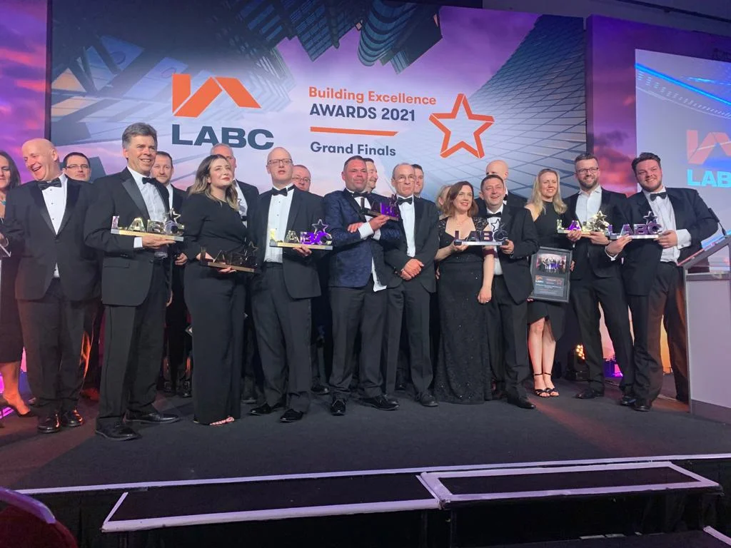 A group of smartly-dressed men and women at an awards ceremony smiling and holding an award